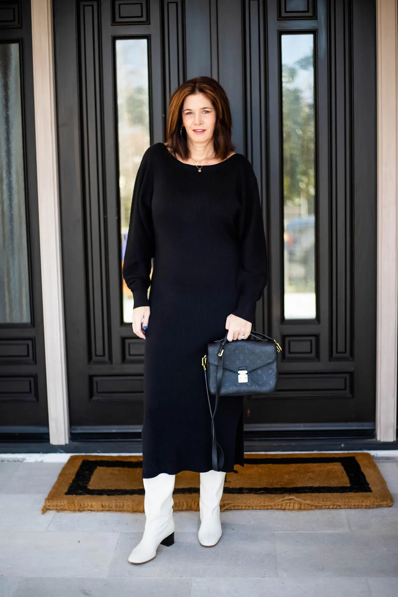 Woman wearing a black ribbed midi sweater dress with white knee-high boots and a black handbag