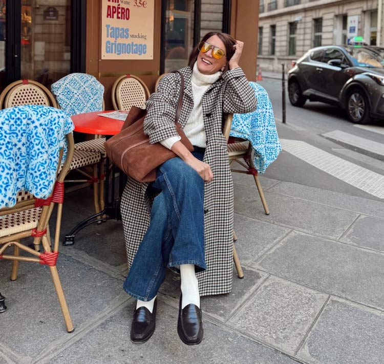 Woman in a black-and-white checked coat with a white sweater, blue jeans and loafers