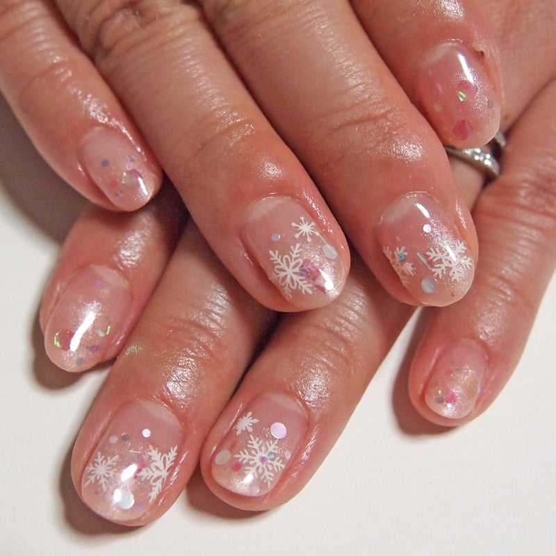 Short sheer nude nails with white snowflakes and scattered glitter dots