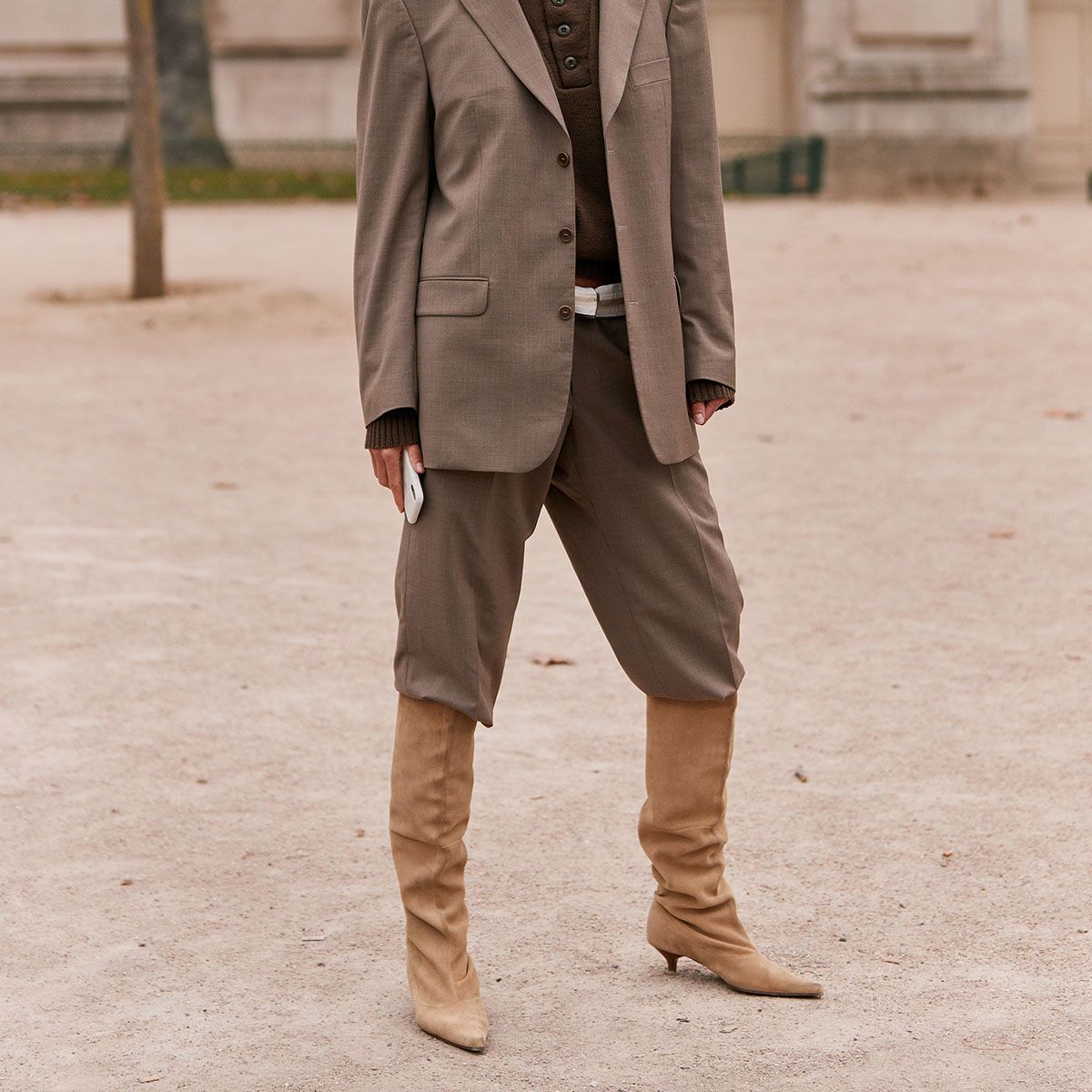 Cropped view of tan suede slouchy boots with taupe trousers and an oversized beige blazer