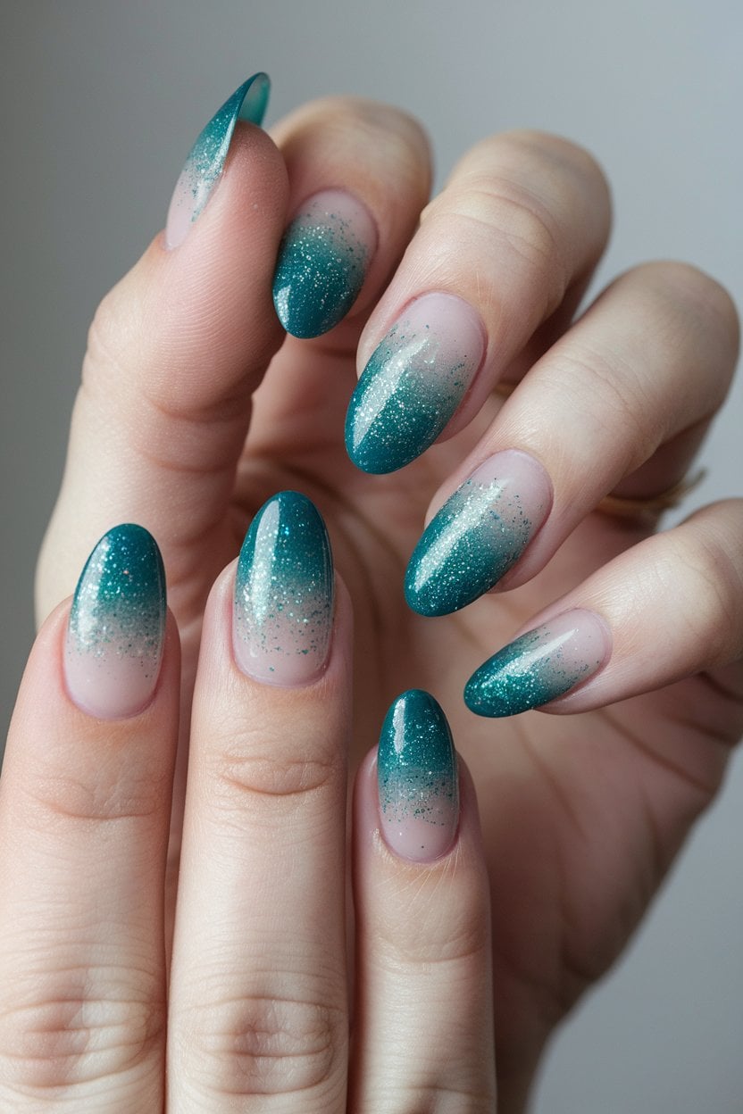 Almond nails with a teal glitter ombré fading from a nude base to deep teal tips; real photography.