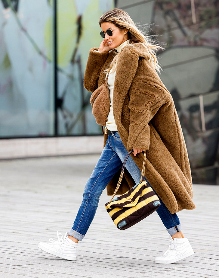 Woman in a caramel teddy coat with a white turtleneck, skinny jeans and white sneakers