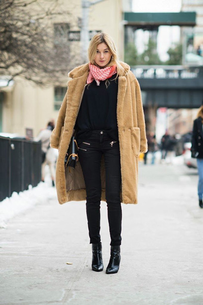 Woman in a camel teddy coat with a pink scarf, black top, black skinny jeans and black ankle boots