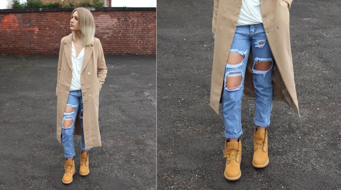 Woman wearing a long camel coat, white top, ripped blue jeans, and wheat Timberland boots