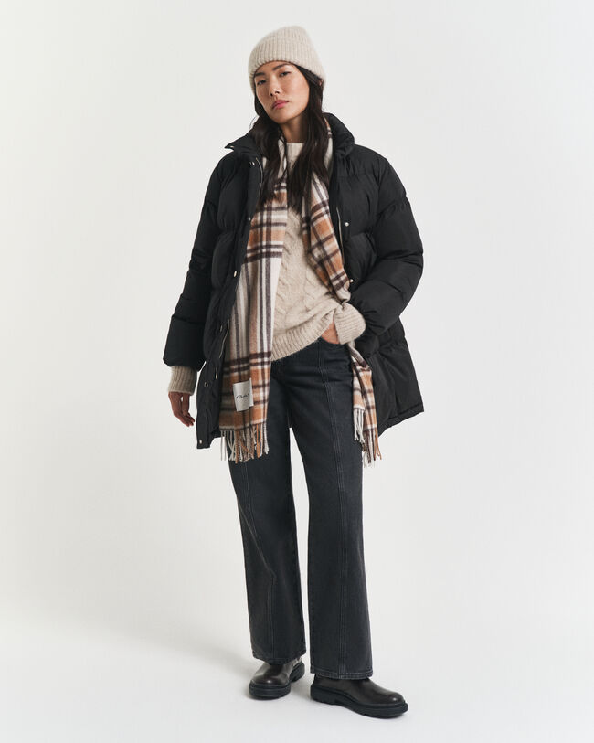 Woman in a black hooded puffer with a cream beanie, cream cable knit, tan plaid scarf, dark wide-leg jeans and black shoes