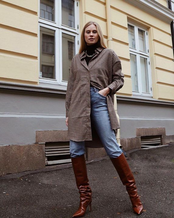 woman in houndstooth long shirt, jeans and brown heeled knee-high boots