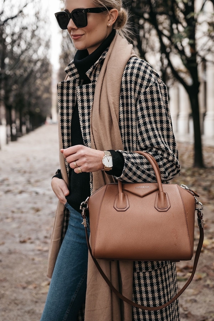 Woman in a camel scarf, black turtleneck, houndstooth coat, jeans and a tan leather bag