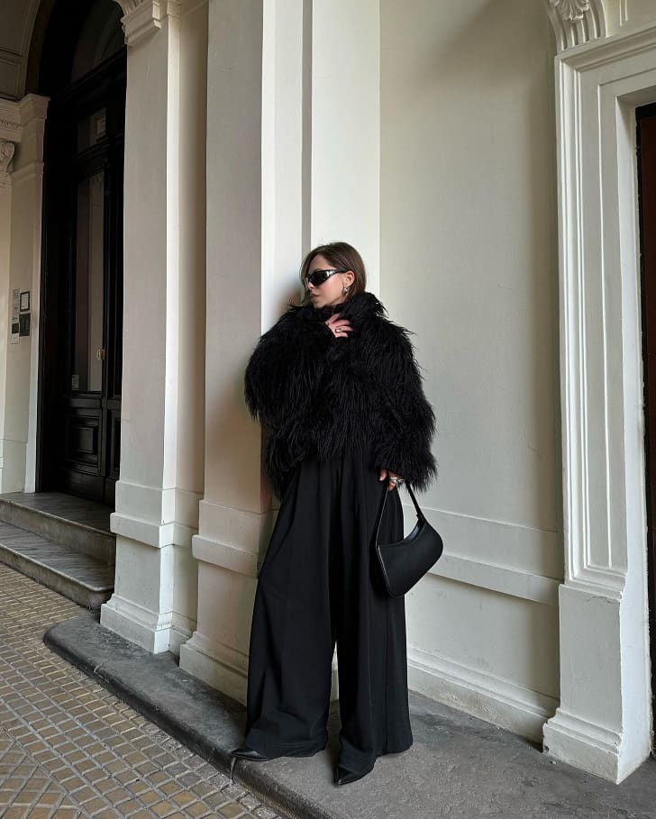 Woman in a black faux-fur collar coat with black wide-leg palazzo trousers and ankle boots