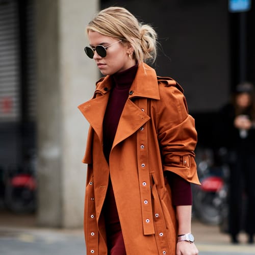 Woman in a burgundy turtleneck with a rust-orange trench coat and sunglasses