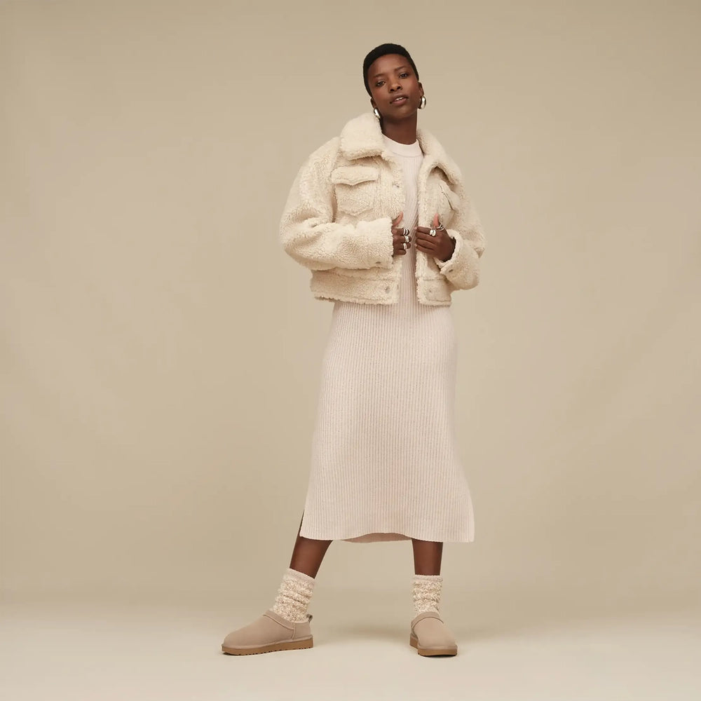 Woman wearing a cream sherpa jacket over a ribbed knit midi dress with knit socks and beige boots