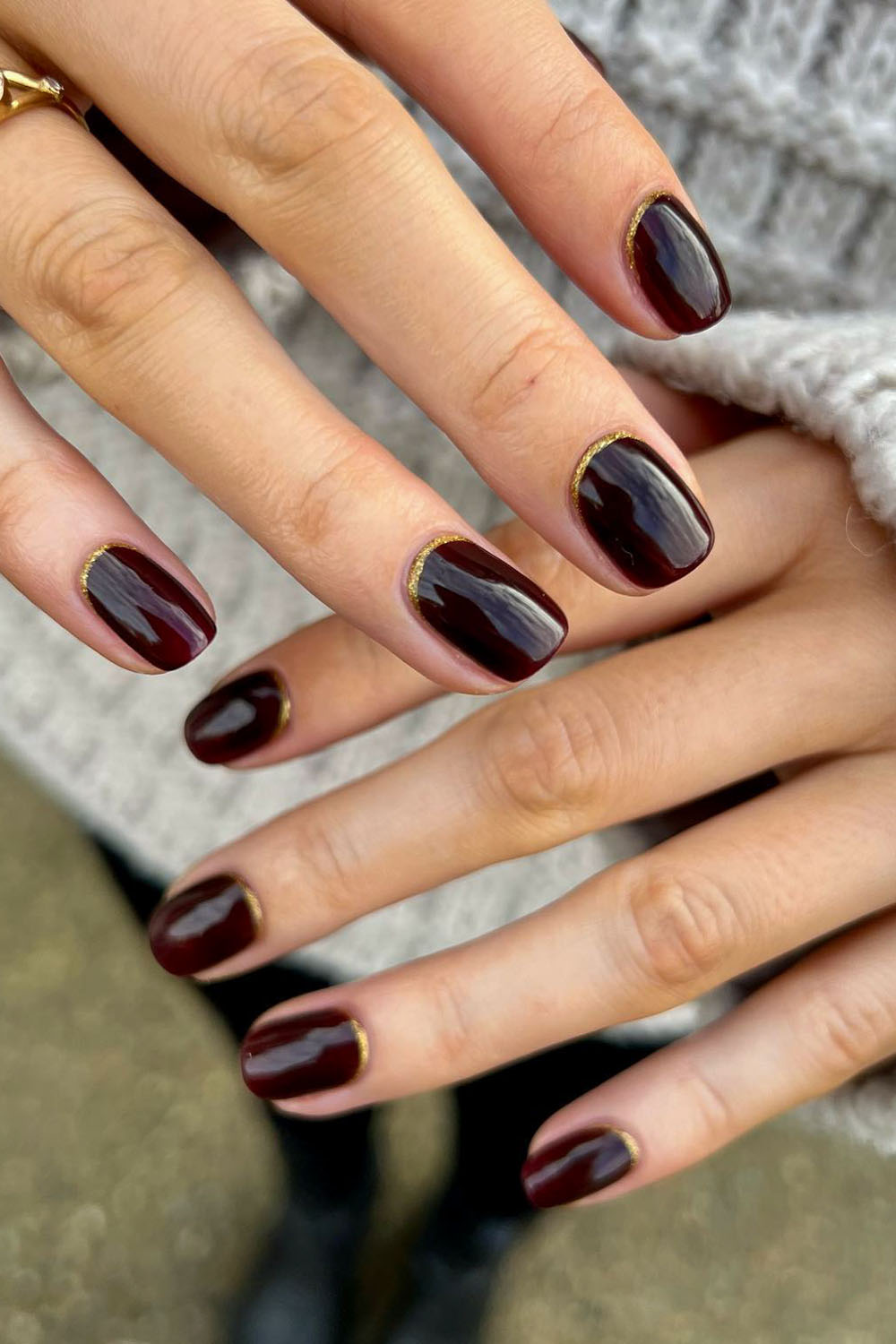 Wine red oval nails with a thin gold outline tracing the cuticle