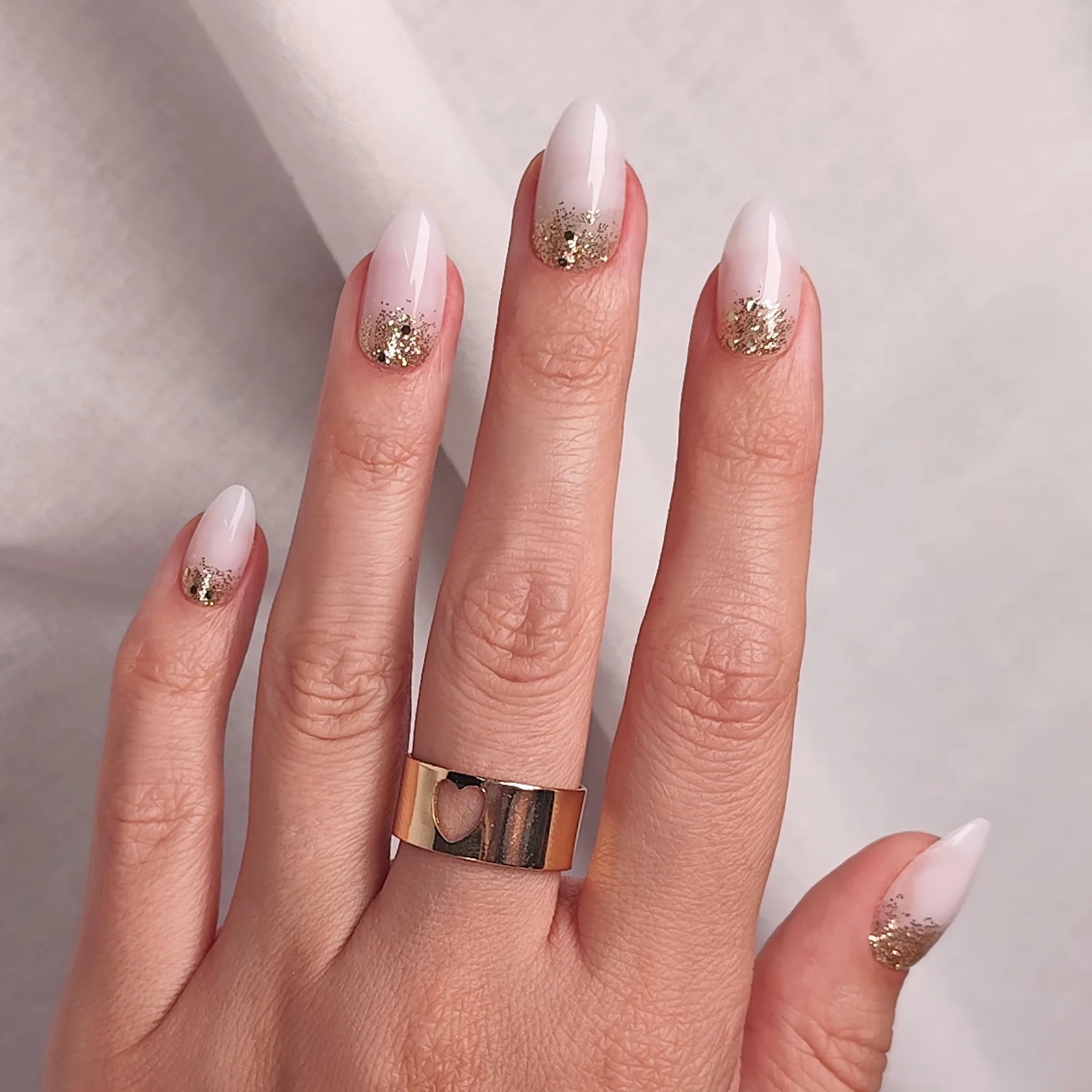 Milky white almond nails with gold glitter at the cuticles