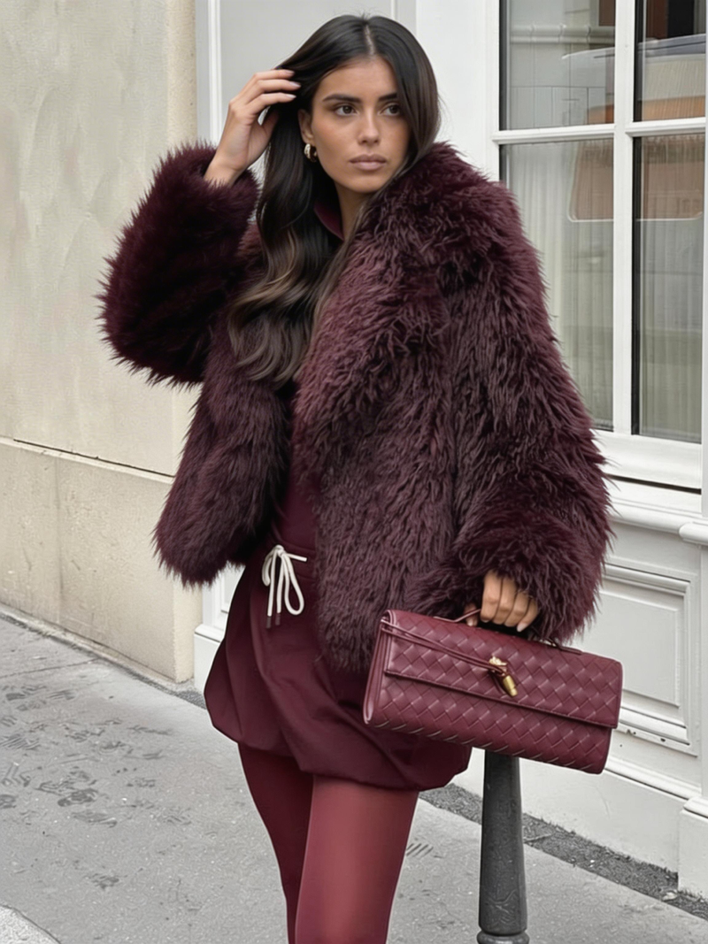 A long-pile burgundy faux fur jacket worn with a burgundy drawstring skirt, burgundy tights and a quilted burgundy handbag.
