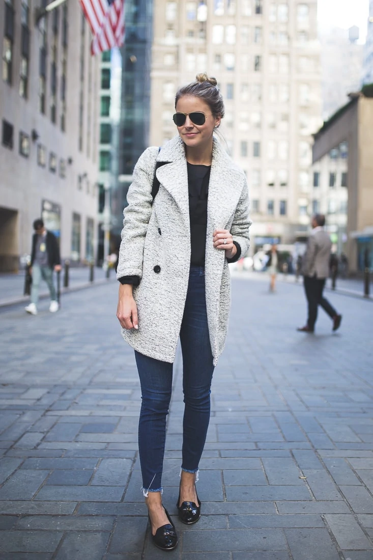 Woman wearing a grey marled wool peacoat with a black top, dark skinny jeans and black loafers