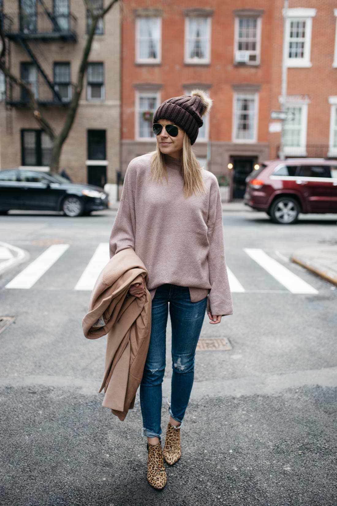 Woman in a brown pom beanie, beige sweater, skinny jeans and leopard booties