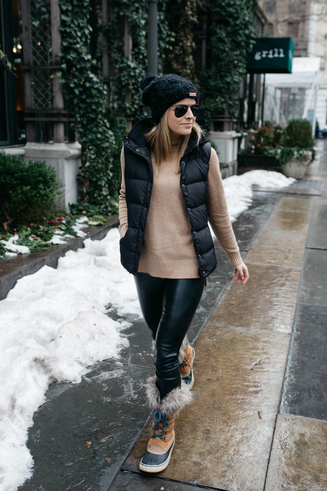 Woman wearing a black puffer vest over a camel turtleneck with Sorel snow boots