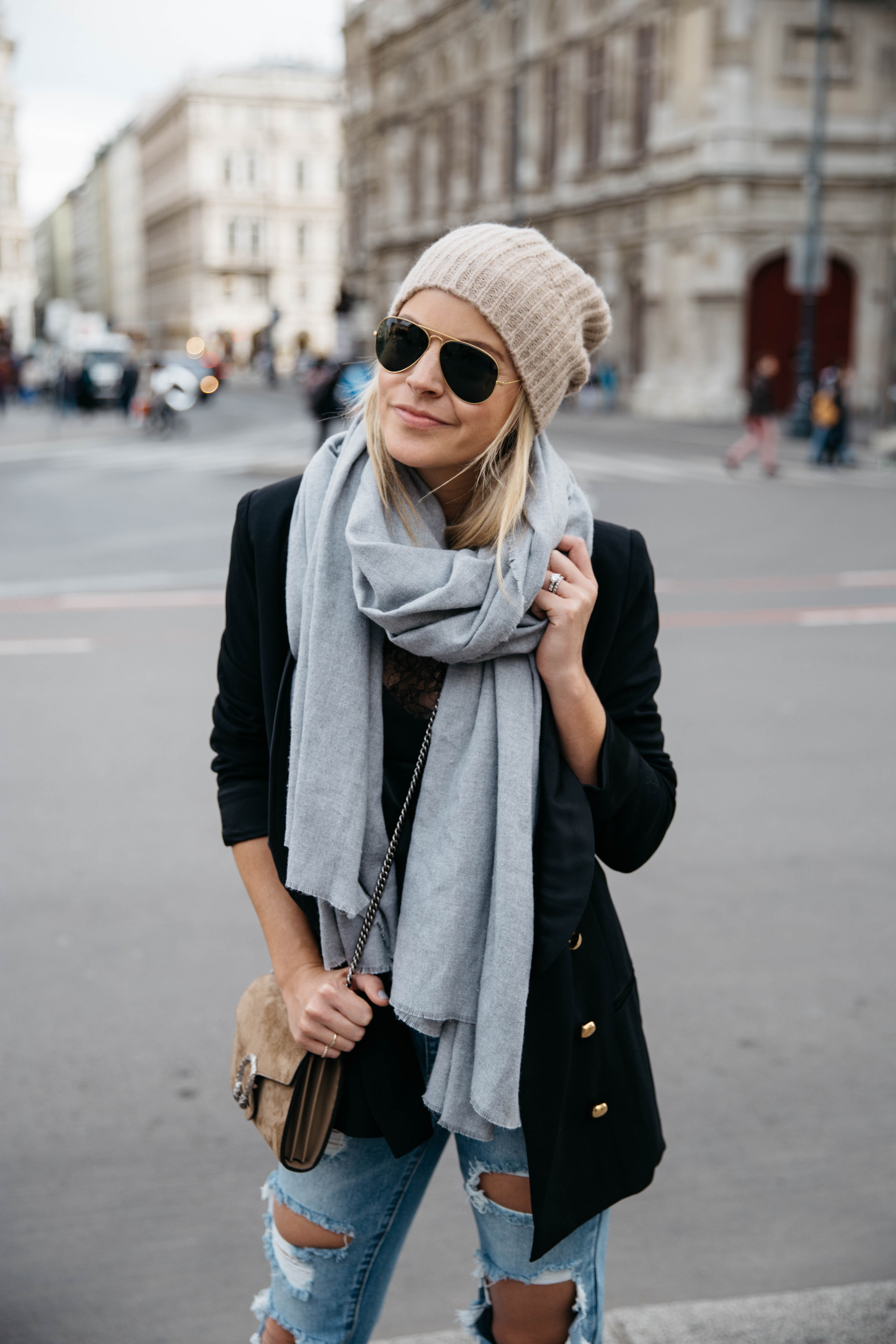 Woman in a beige beanie, grey scarf, black blazer and ripped jeans