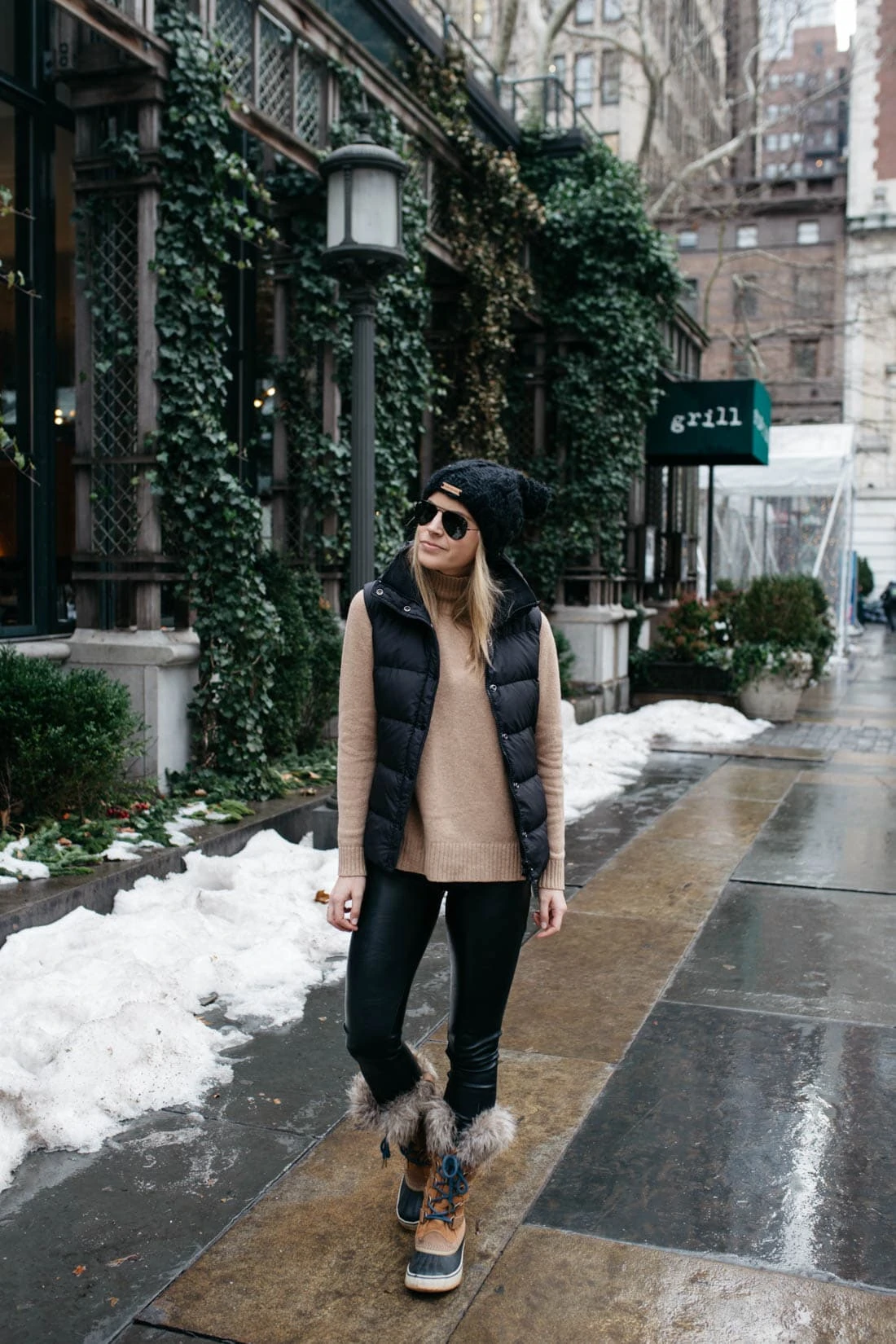 Full-length street photo of a woman in a puffer vest, leggings and fur-trim Sorel boots