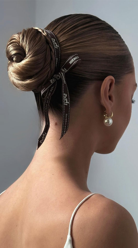 Sleek ballerina bun with a black ribbon bow headband detail, brown hair. Note: the detail is a ribbon bow rather than a twisted fabric headb