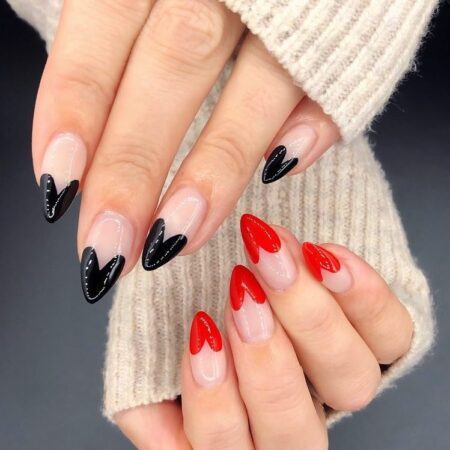 Short almond nails with a sheer nude base and heart-shaped french tips alternating glossy black and red
