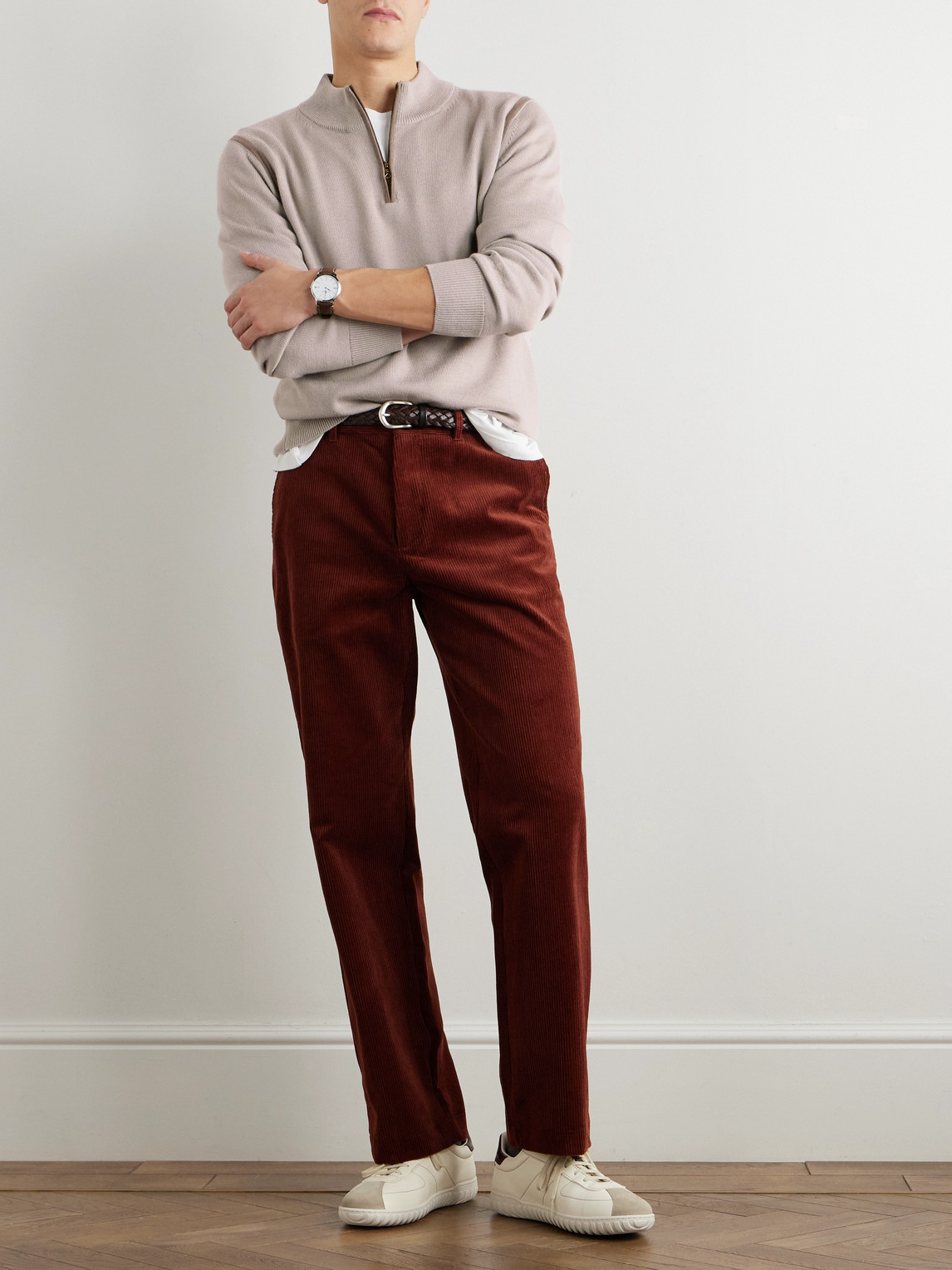 Man wearing a beige quarter-zip sweater with rust corduroy trousers and white sneakers