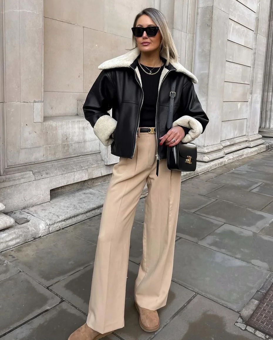 Woman wearing a black shearling aviator jacket with beige pleated wide-leg trousers