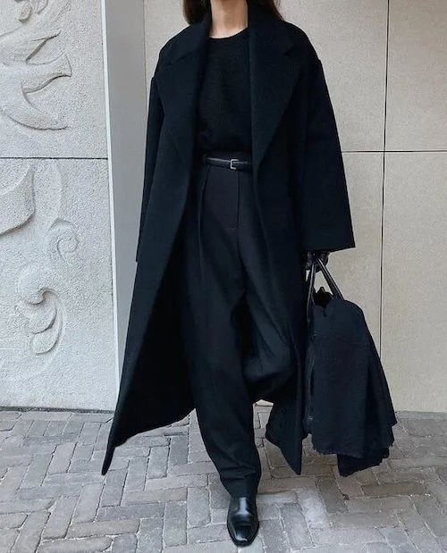 Woman in a black maxi coat with black top, black wide-leg trousers, belt and black loafers