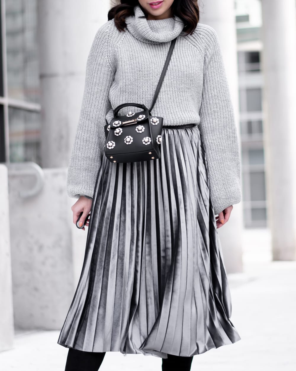 Woman in a grey chunky turtleneck sweater with a silver pleated midi skirt