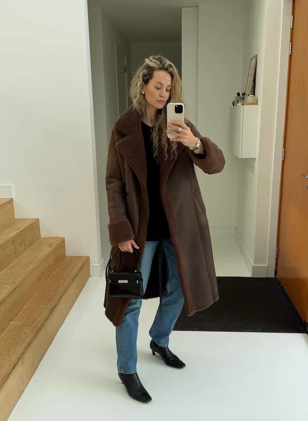 Woman wearing a long brown coat with jeans and booties