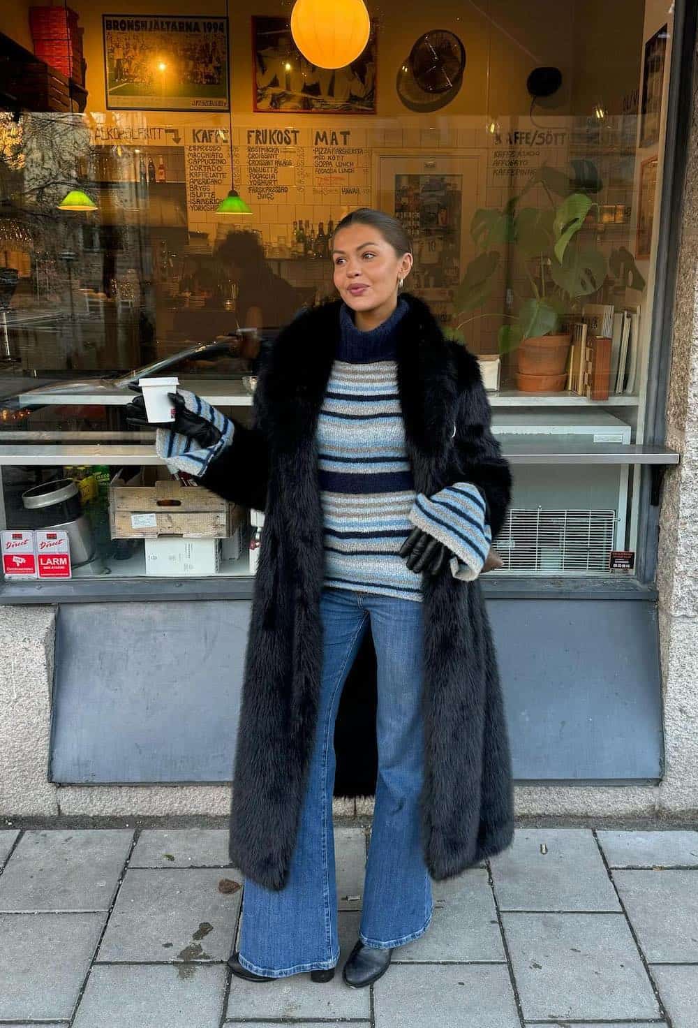 Woman wearing a long faux fur coat with flare jeans and a striped sweater