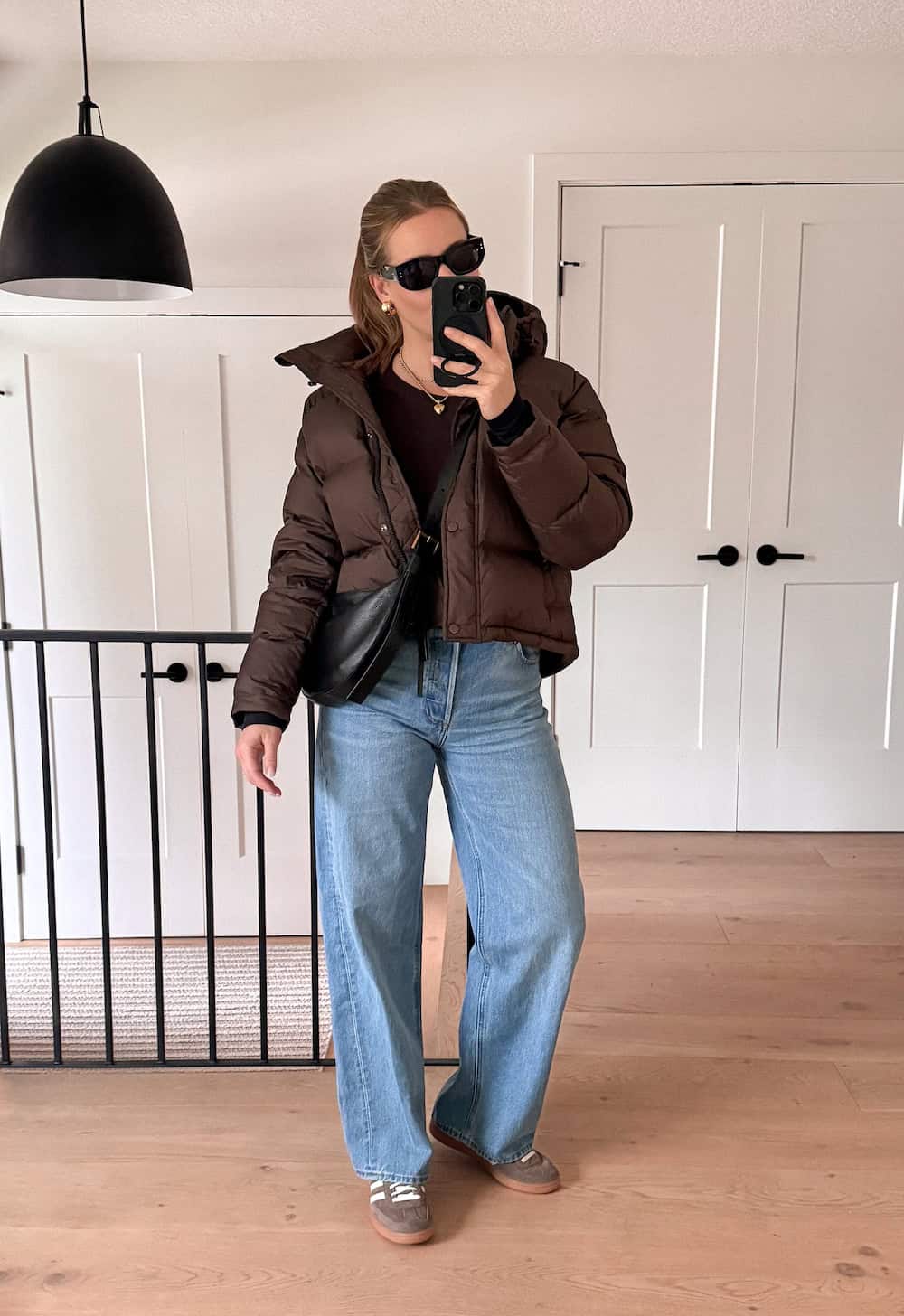 Woman wearing a chocolate brown puffer jacket with baggy blue jeans and brown sneakers