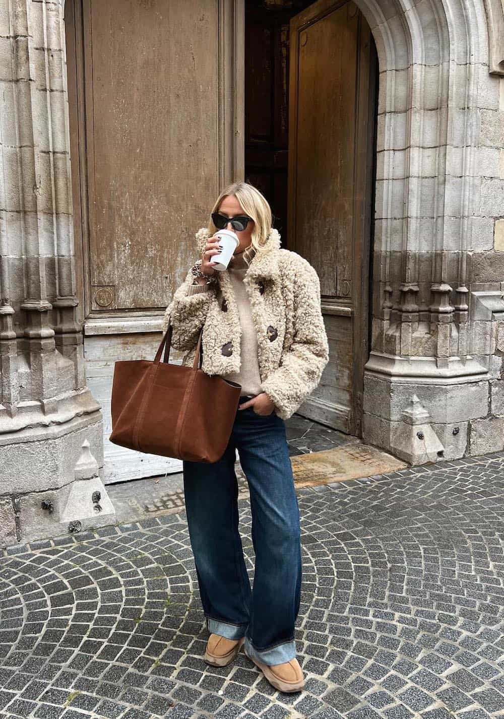 Woman wearing a faux shearling teddy jacket with cuffed jeans, a sweater and Ugg boots