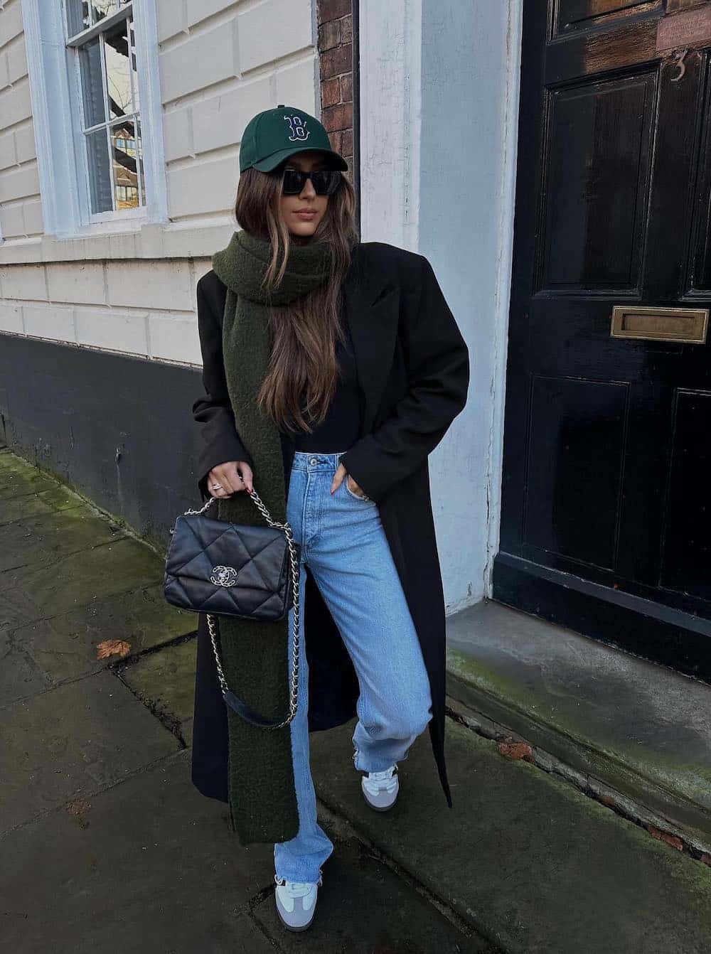 Woman wearing a long black coat with jeans and sneakers with green accents