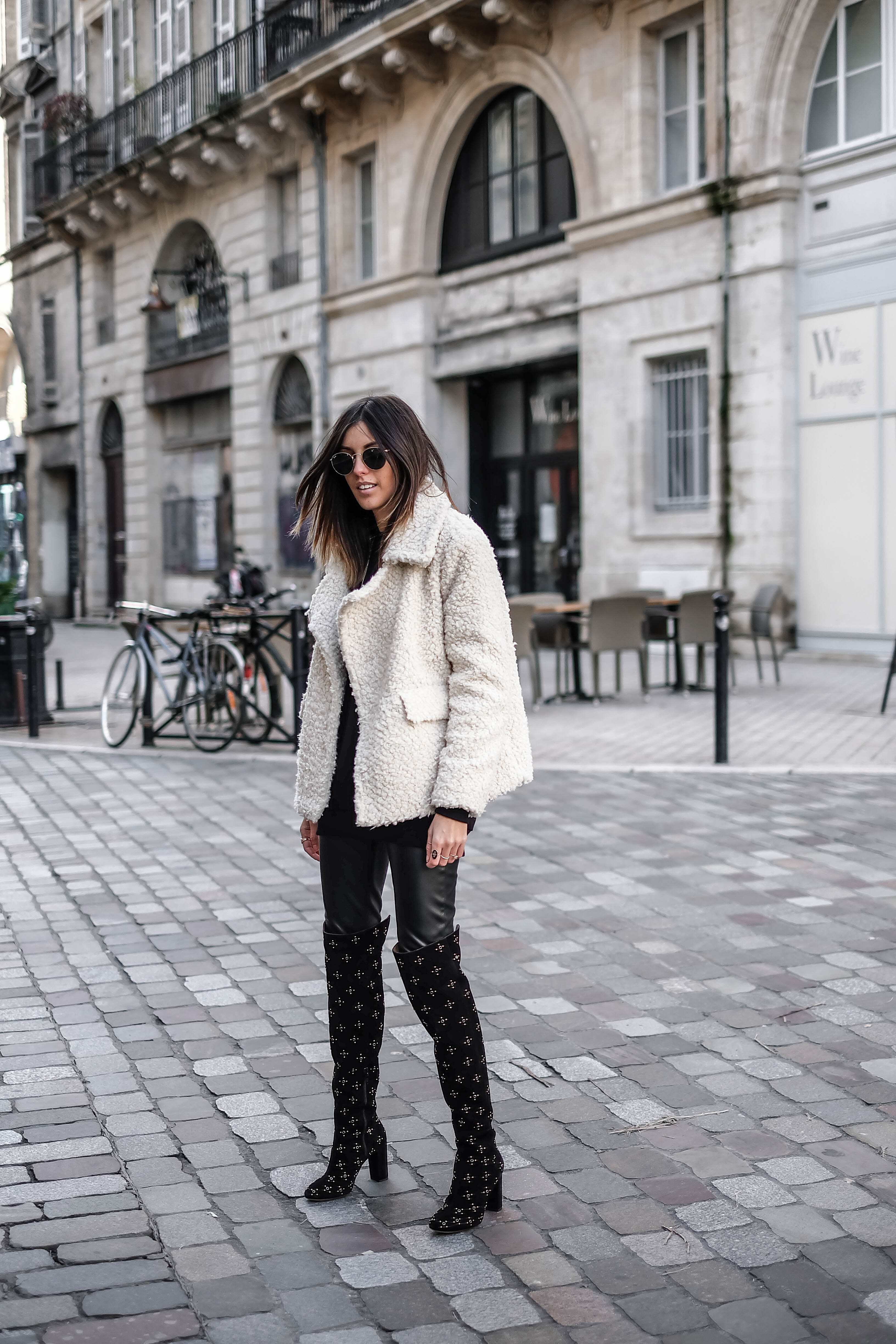 White shearling coat with black leather leggings and studded over-the-knee boots