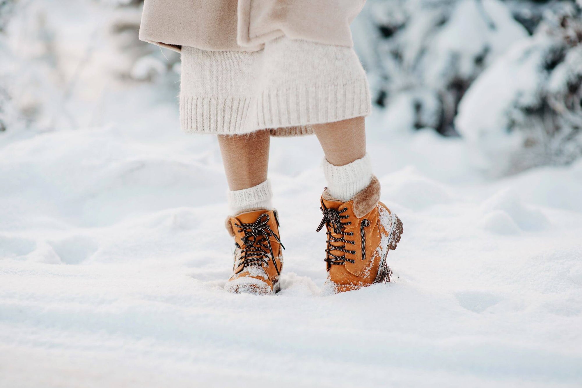 Close-up of tan lace-up snow boots with white knit socks and a sweater dress in deep snow