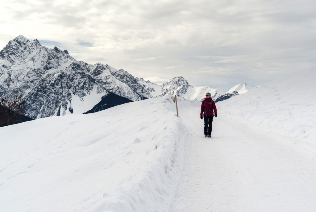 Woman in a red insulated jacket walking a groomed snowy alpine path