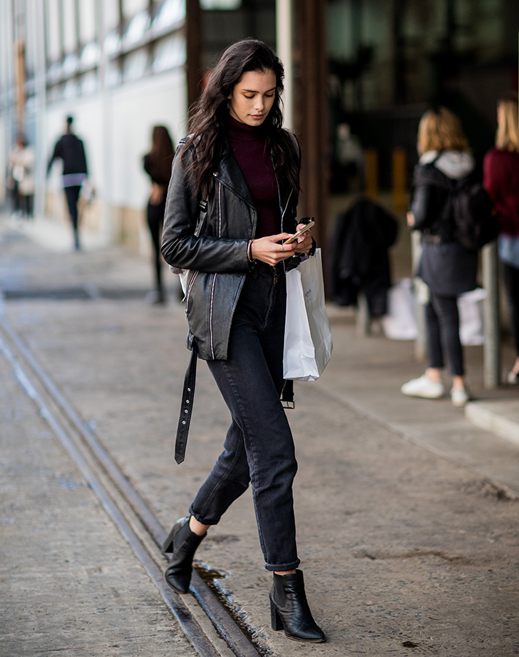 Woman in a black leather jacket, burgundy turtleneck, black jeans and black heeled ankle boots