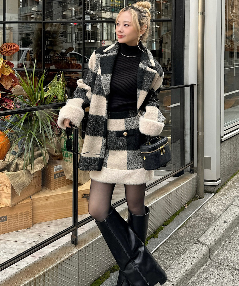 Woman in a black and cream checkered wool coat with matching mini skirt, black turtleneck and knee-high boots